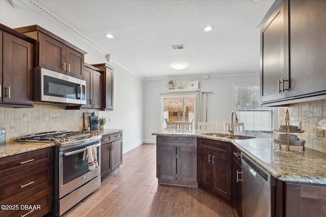 kitchen featuring visible vents, ornamental molding, light stone counters, a sink, and stainless steel appliances