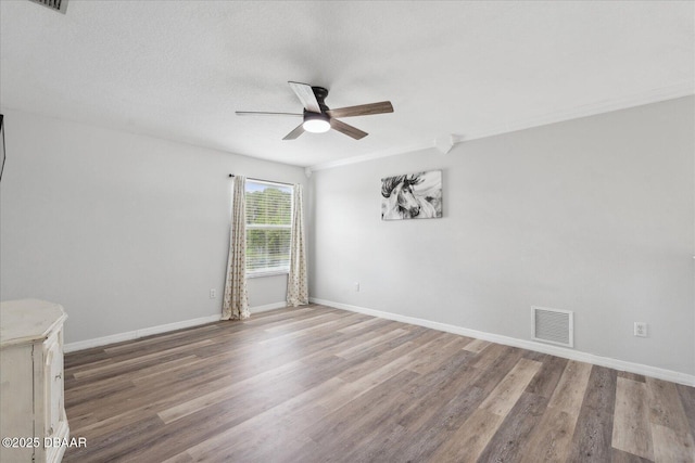 spare room with visible vents, a ceiling fan, baseboards, and wood finished floors