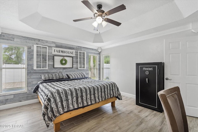 bedroom featuring ceiling fan, crown molding, a raised ceiling, baseboards, and light wood-style flooring