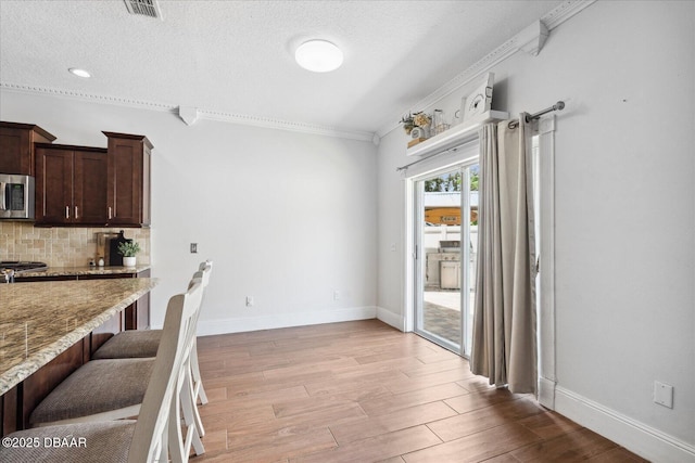 unfurnished dining area with crown molding, visible vents, light wood-style floors, baseboards, and a textured ceiling