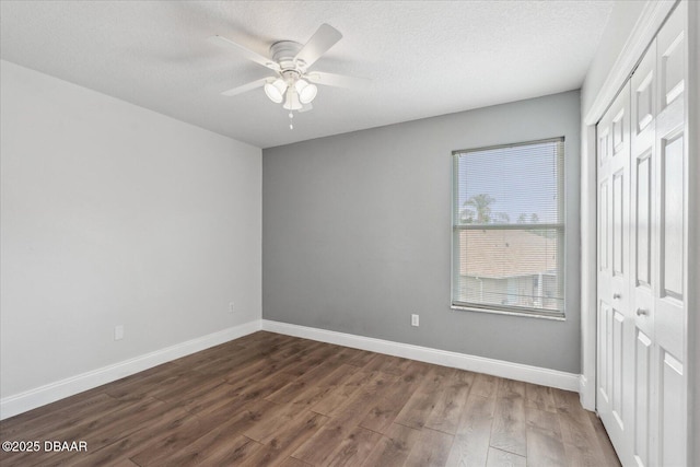 unfurnished bedroom with baseboards, a closet, dark wood-style flooring, and a textured ceiling