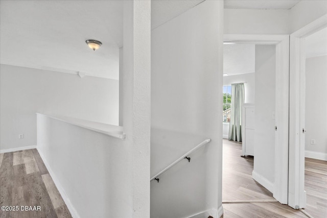 hallway featuring baseboards, wood finished floors, and an upstairs landing