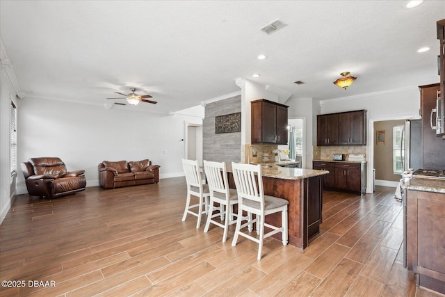 kitchen with ceiling fan, visible vents, a peninsula, open floor plan, and ornamental molding