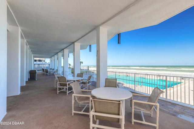 view of patio with a community pool, a water view, and a beach view