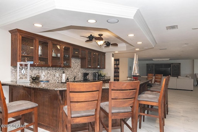 bar with tasteful backsplash, ceiling fan, a raised ceiling, crown molding, and dark brown cabinets