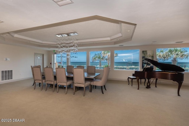 dining area with a raised ceiling, crown molding, a water view, and carpet flooring