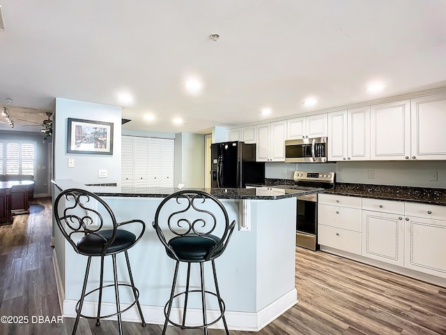 kitchen with a kitchen bar, wood-type flooring, white cabinets, and appliances with stainless steel finishes