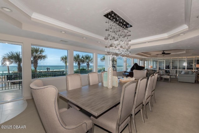 dining space with a water view, ornamental molding, and a tray ceiling