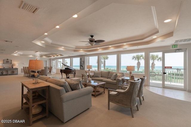 carpeted living room featuring a tray ceiling, a wealth of natural light, and a water view