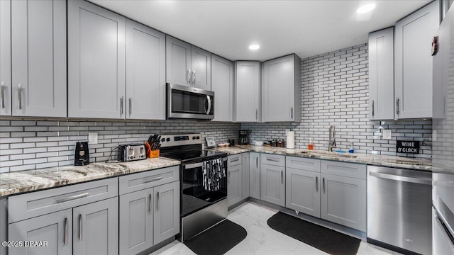 kitchen featuring gray cabinets, a sink, stainless steel appliances, marble finish floor, and backsplash