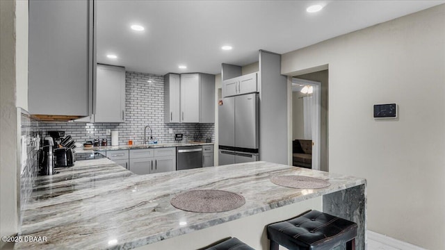 kitchen featuring light stone countertops, a peninsula, a sink, decorative backsplash, and stainless steel appliances