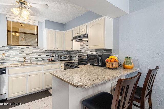 kitchen featuring a sink, under cabinet range hood, light stone countertops, black appliances, and a kitchen breakfast bar