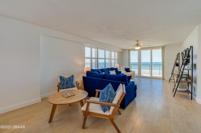 living area with baseboards, a water view, light wood-style floors, and a ceiling fan