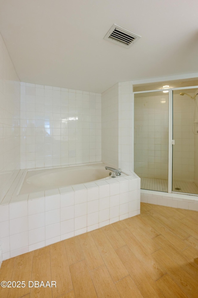 full bathroom with visible vents, a shower stall, a garden tub, and wood finished floors