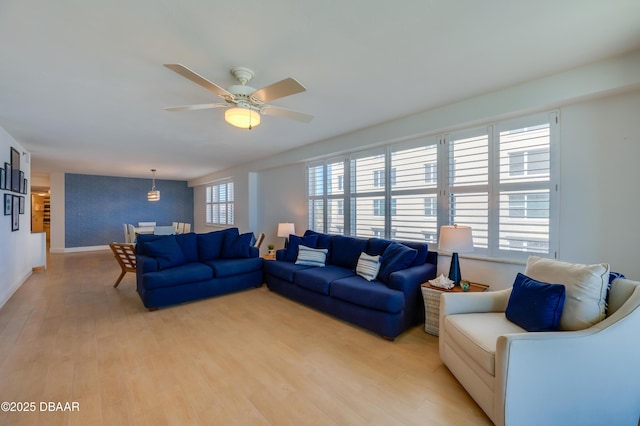 living area with baseboards, light wood-type flooring, and ceiling fan