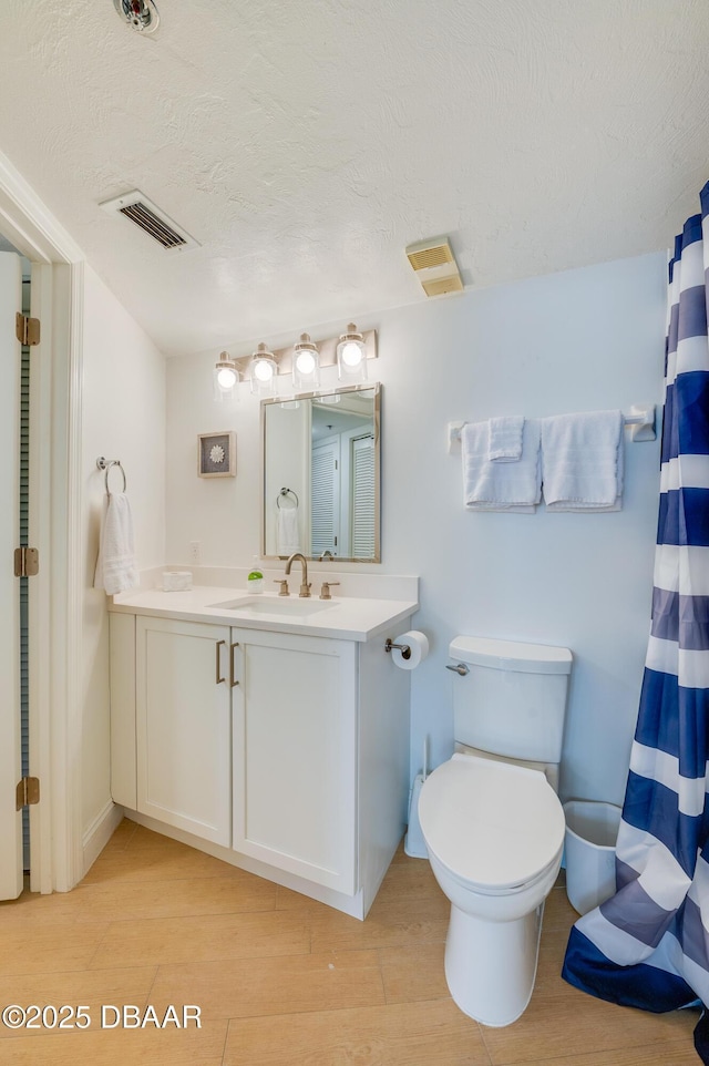 bathroom featuring visible vents, toilet, vanity, wood finished floors, and a textured ceiling