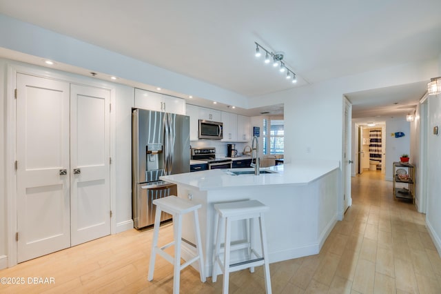 kitchen featuring a peninsula, a sink, stainless steel appliances, white cabinetry, and a kitchen bar