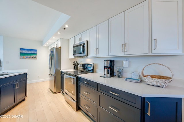 kitchen featuring recessed lighting, a sink, light countertops, appliances with stainless steel finishes, and white cabinetry