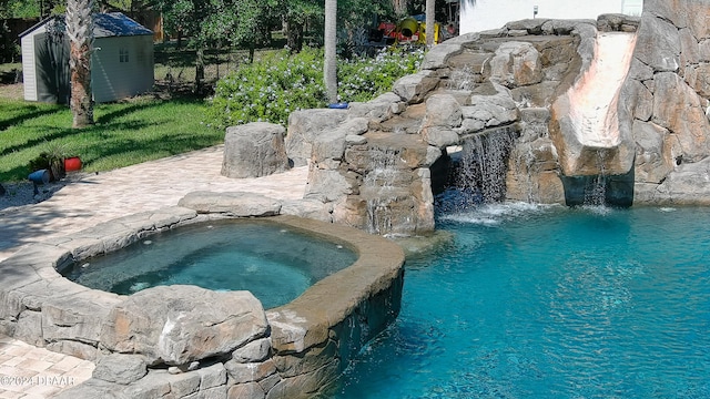 view of swimming pool featuring pool water feature, a storage unit, and an in ground hot tub