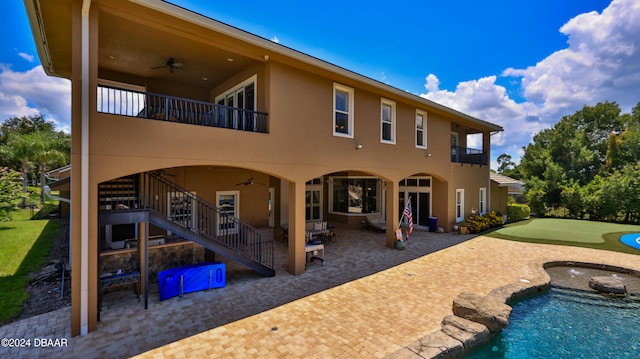 rear view of property with ceiling fan, a swimming pool with hot tub, a patio area, and a balcony