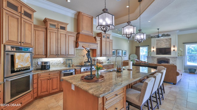 kitchen with hanging light fixtures, a brick fireplace, a kitchen breakfast bar, an island with sink, and appliances with stainless steel finishes