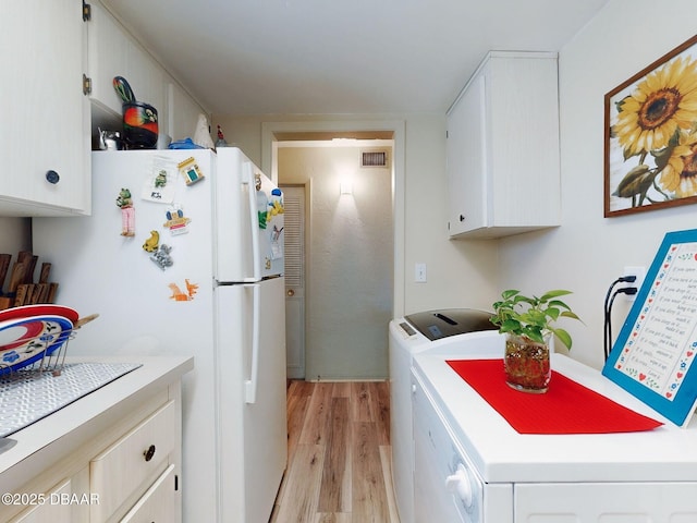 kitchen with washing machine and clothes dryer, visible vents, light countertops, white cabinets, and light wood-style floors