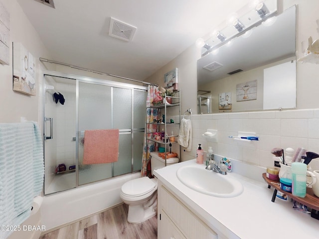 bathroom with visible vents, wood finished floors, vanity, combined bath / shower with glass door, and toilet
