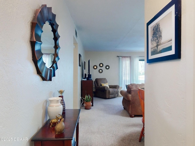 hallway with a textured wall, carpet flooring, and visible vents