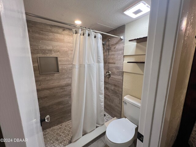 bathroom with walk in shower, a textured ceiling, wood walls, tile patterned flooring, and toilet