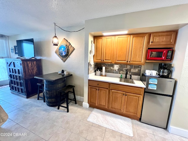 kitchen featuring light tile patterned flooring, sink, tasteful backsplash, a textured ceiling, and stainless steel fridge