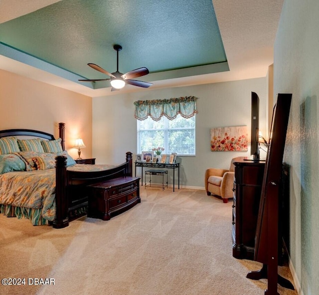 bedroom with a textured ceiling, light carpet, ceiling fan, and a tray ceiling