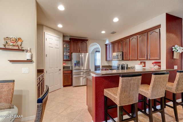 kitchen with a kitchen bar, kitchen peninsula, light tile patterned floors, sink, and appliances with stainless steel finishes