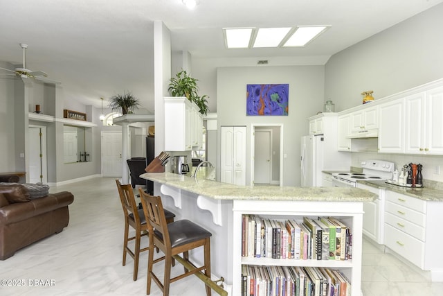 kitchen featuring open floor plan, a kitchen bar, a peninsula, white appliances, and a ceiling fan