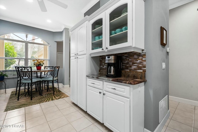 kitchen featuring white cabinets, decorative backsplash, dark stone countertops, ornamental molding, and light tile patterned flooring