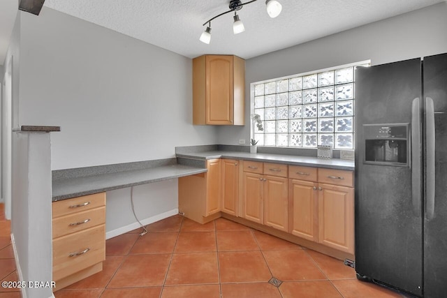 kitchen with built in desk, light tile patterned floors, black refrigerator with ice dispenser, light brown cabinetry, and a textured ceiling