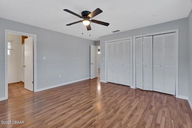 unfurnished bedroom with two closets, visible vents, baseboards, and wood finished floors