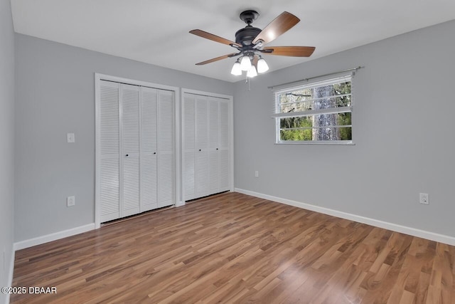 unfurnished bedroom featuring ceiling fan, baseboards, multiple closets, and wood finished floors