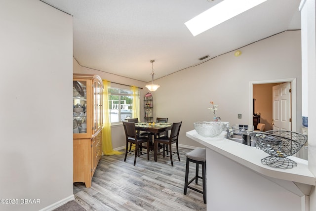 dining room featuring light hardwood / wood-style floors and vaulted ceiling with skylight