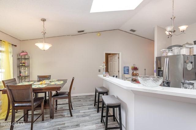 dining area with vaulted ceiling with skylight, light wood-type flooring, and an inviting chandelier