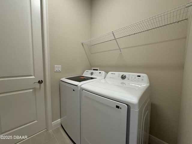 clothes washing area with washer and dryer, laundry area, light tile patterned floors, and baseboards