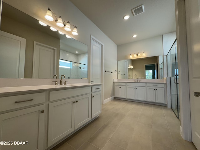 bathroom featuring visible vents, two vanities, a stall shower, a sink, and recessed lighting