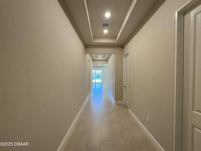 hall featuring a tray ceiling, recessed lighting, visible vents, and baseboards