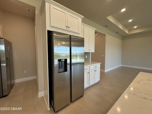 kitchen featuring light stone counters, visible vents, and stainless steel fridge