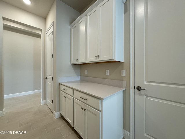 interior space featuring baseboards, white cabinets, and light countertops