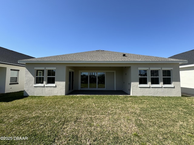 rear view of house with stucco siding, a lawn, and a shingled roof