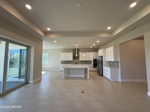 kitchen with visible vents, wall chimney range hood, light countertops, refrigerator with ice dispenser, and recessed lighting