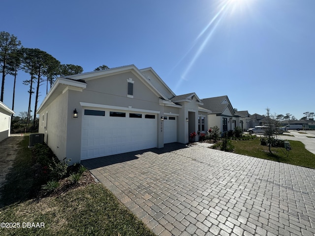 view of front of property with decorative driveway, cooling unit, a garage, and stucco siding