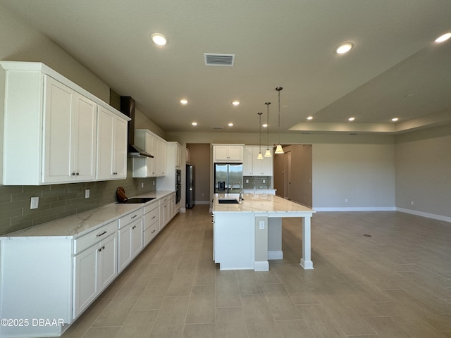 kitchen featuring visible vents, stainless steel refrigerator with ice dispenser, a sink, wall chimney range hood, and black electric stovetop