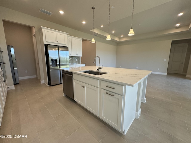 kitchen with visible vents, a tray ceiling, an island with sink, a sink, and appliances with stainless steel finishes