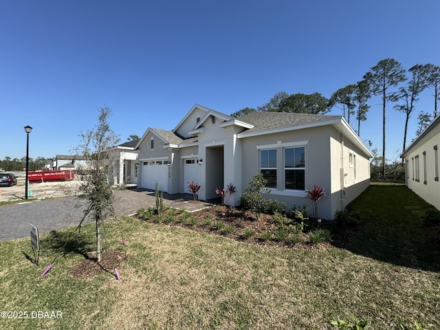 view of front facade featuring stucco siding, a front lawn, decorative driveway, roof with shingles, and a garage